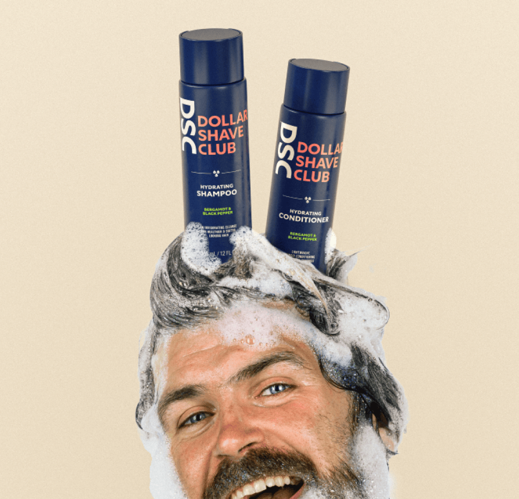 Head of man with soapy lather balancing Dollar Shave Club's Shampoo and Conditioner products on his head.