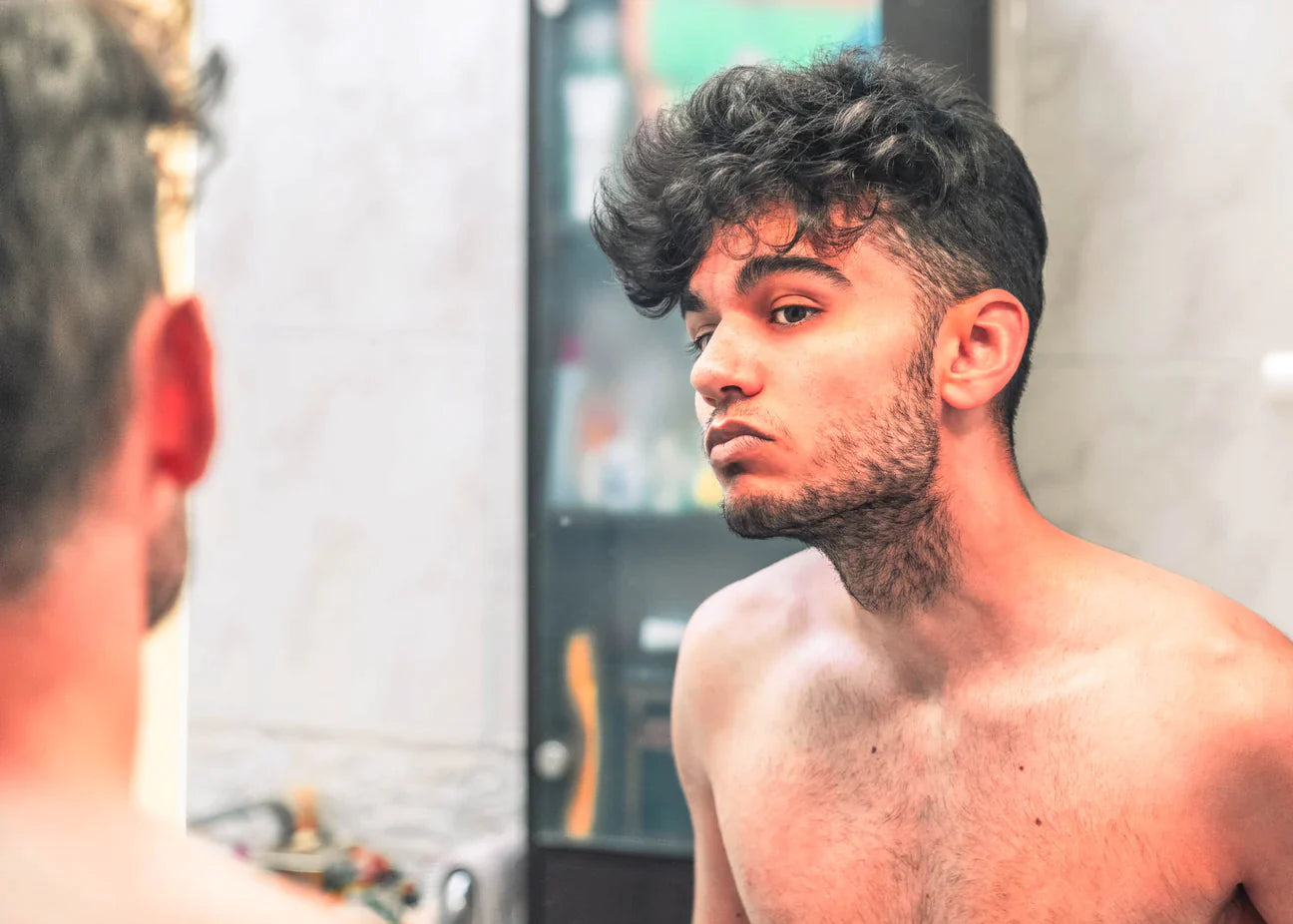 Man looking in mirror at hair and stubble on face.