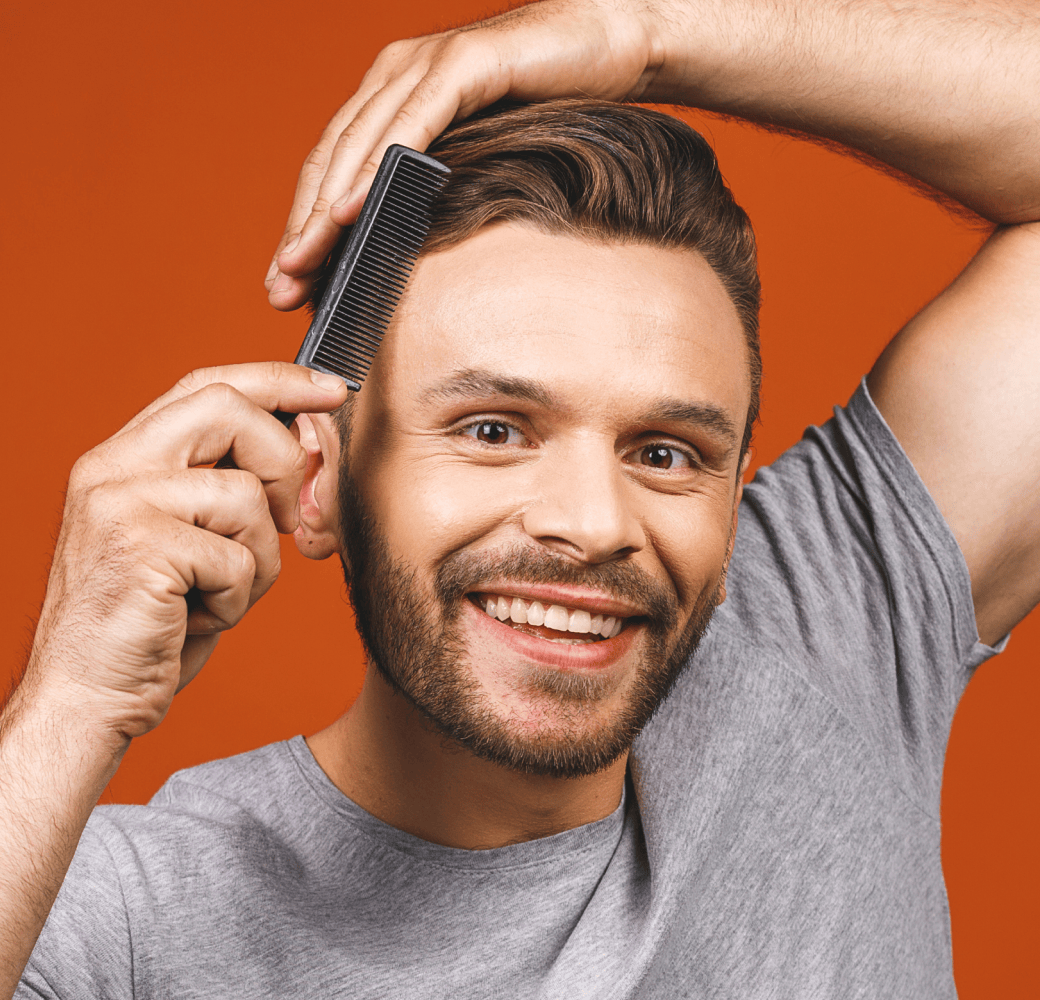 A smiling man styling his hair with a comb.
