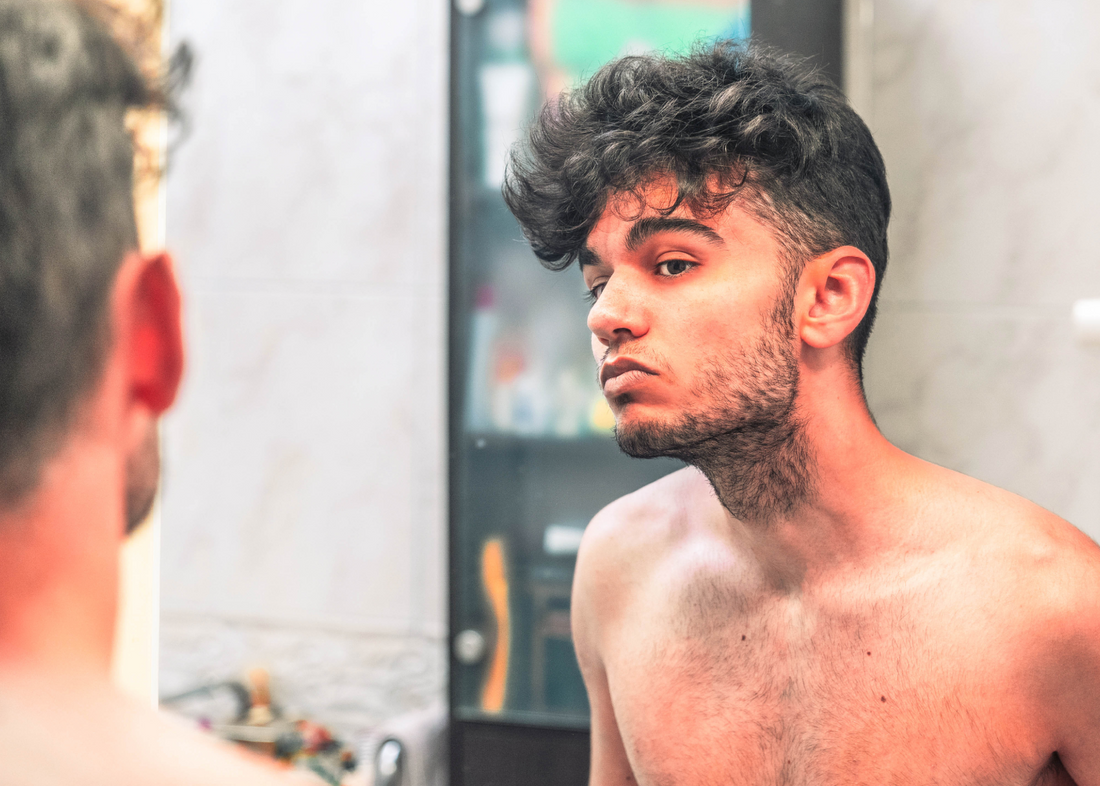 Man looking at shaved face and beard in mirror.