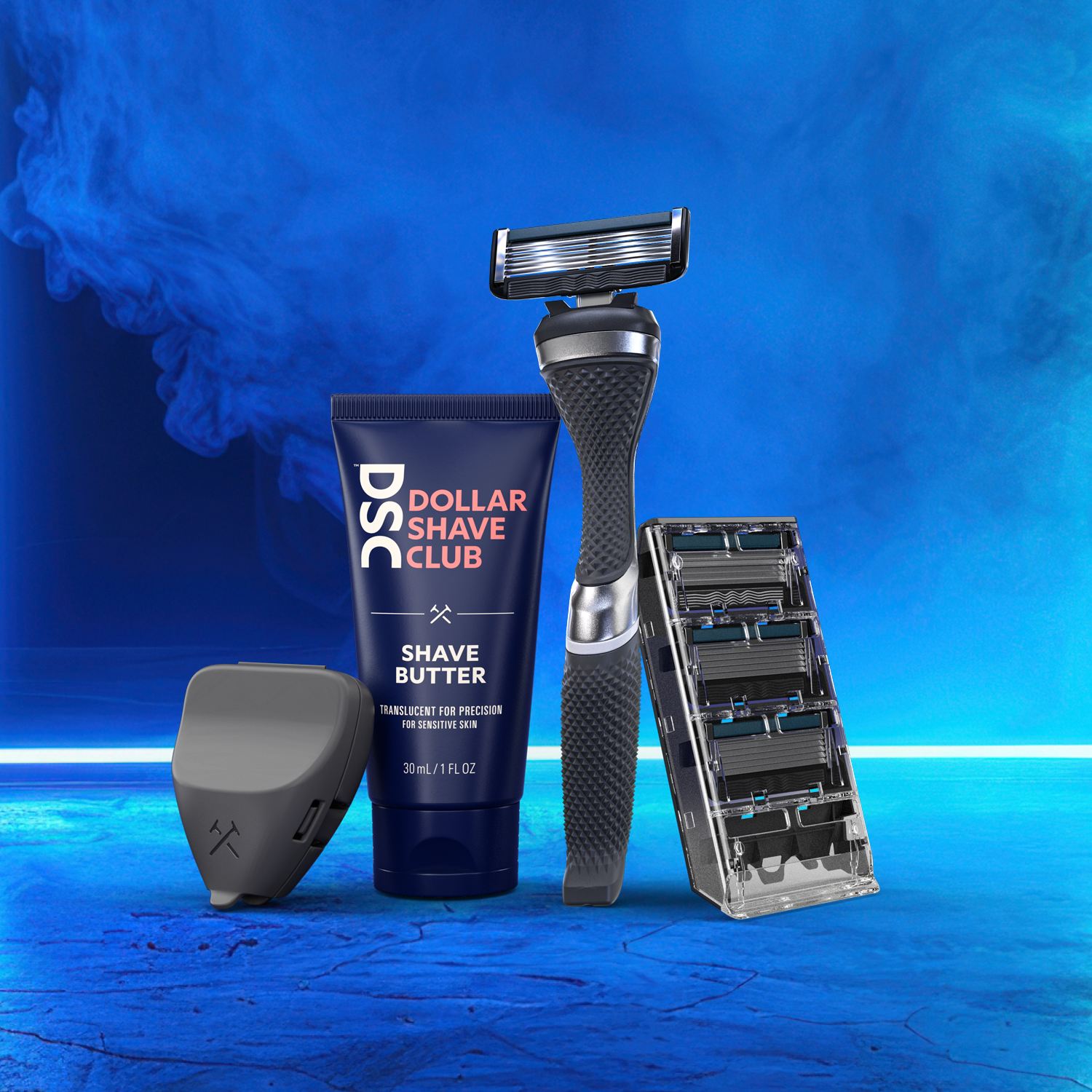 Razor blade and handle, razor cover, and trial size shave butter agains a smokey blue background