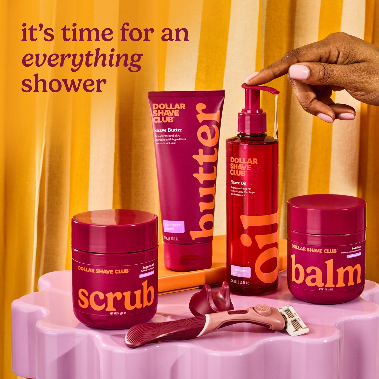 Dollar Shave Club products including scrub, balm, and shave oil on a pink stand with a yellow curtain background.