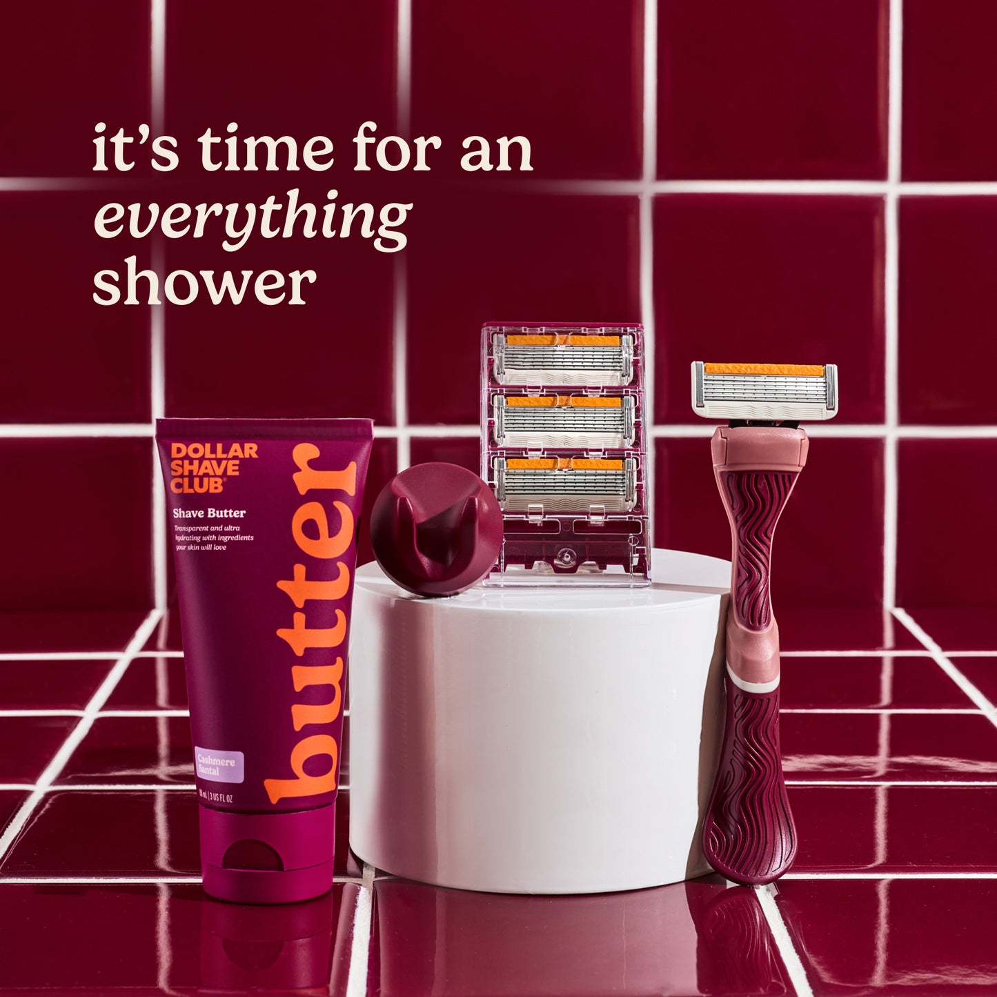 Shaving products including a tube of 'Dollar Shave Club' butter, razors, and razor heads on a red tiled background with text 'it's time for an everything shower'.