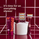 Shaving products including a tube of 'Dollar Shave Club' butter, razors, and razor heads on a red tiled background with text 'it's time for an everything shower'.