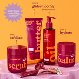 Dollar Shave Club grooming products including scrub, butter, oil, and balm on a pink stand with an orange background.
