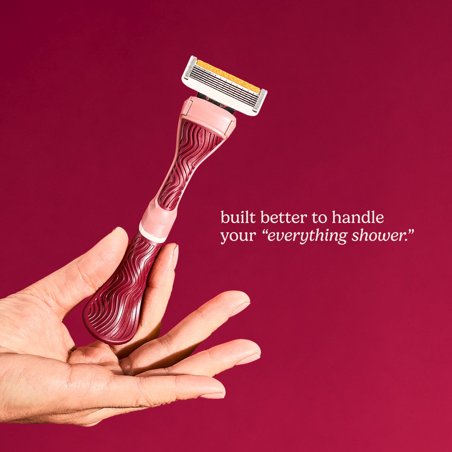 Hand holding a maroon and white razor with words saying "built to handle your "everything shower""