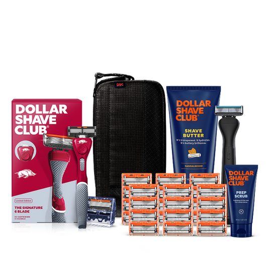 Dollar Shave Club University of Arkansas grooming kit on a white background. Includes a cardinal red razor handle with the Arkansas Razorbacks logo, 24 blades, Shave Butter, Prep Scrub, a black 3-in-1 electric trimmer, and a black traveler case.