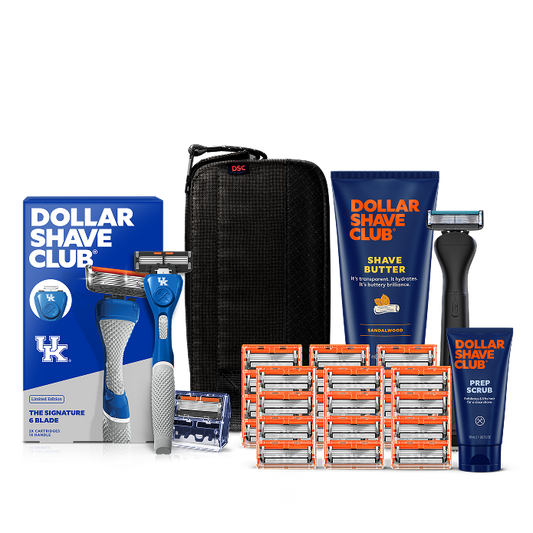Dollar Shave Club University of Kentucky grooming kit on a white background. Includes a royal blue razor handle with the Kentucky Wildcats logo, 24 blades, Shave Butter, Prep Scrub, a black 3-in-1 electric trimmer, and a black traveler case.
