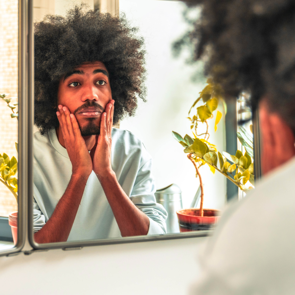 man touching face and looking in a mirror