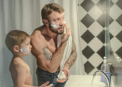 father showing son how to apply shaving cream in bathroom