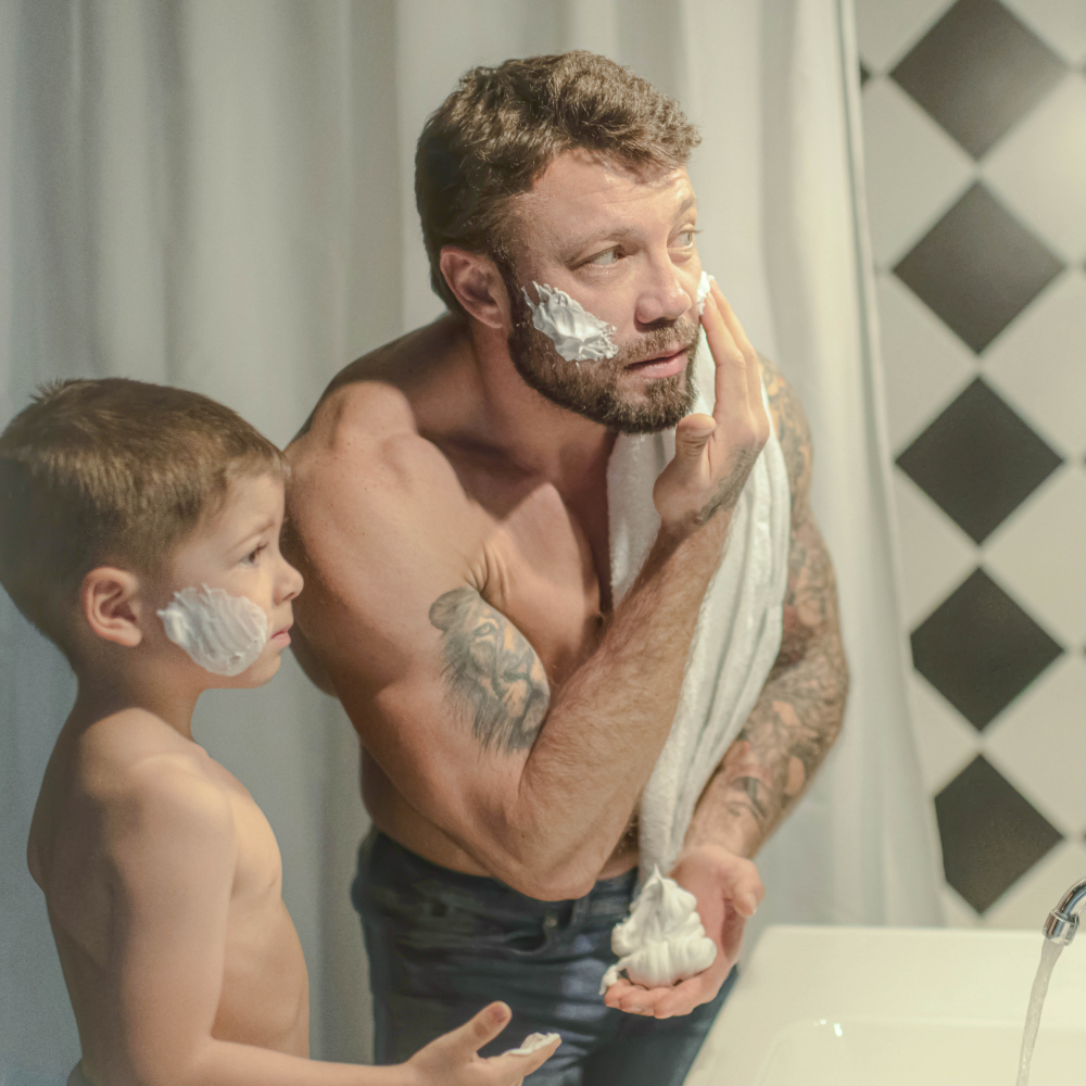Man shaving looking in mirror with son.